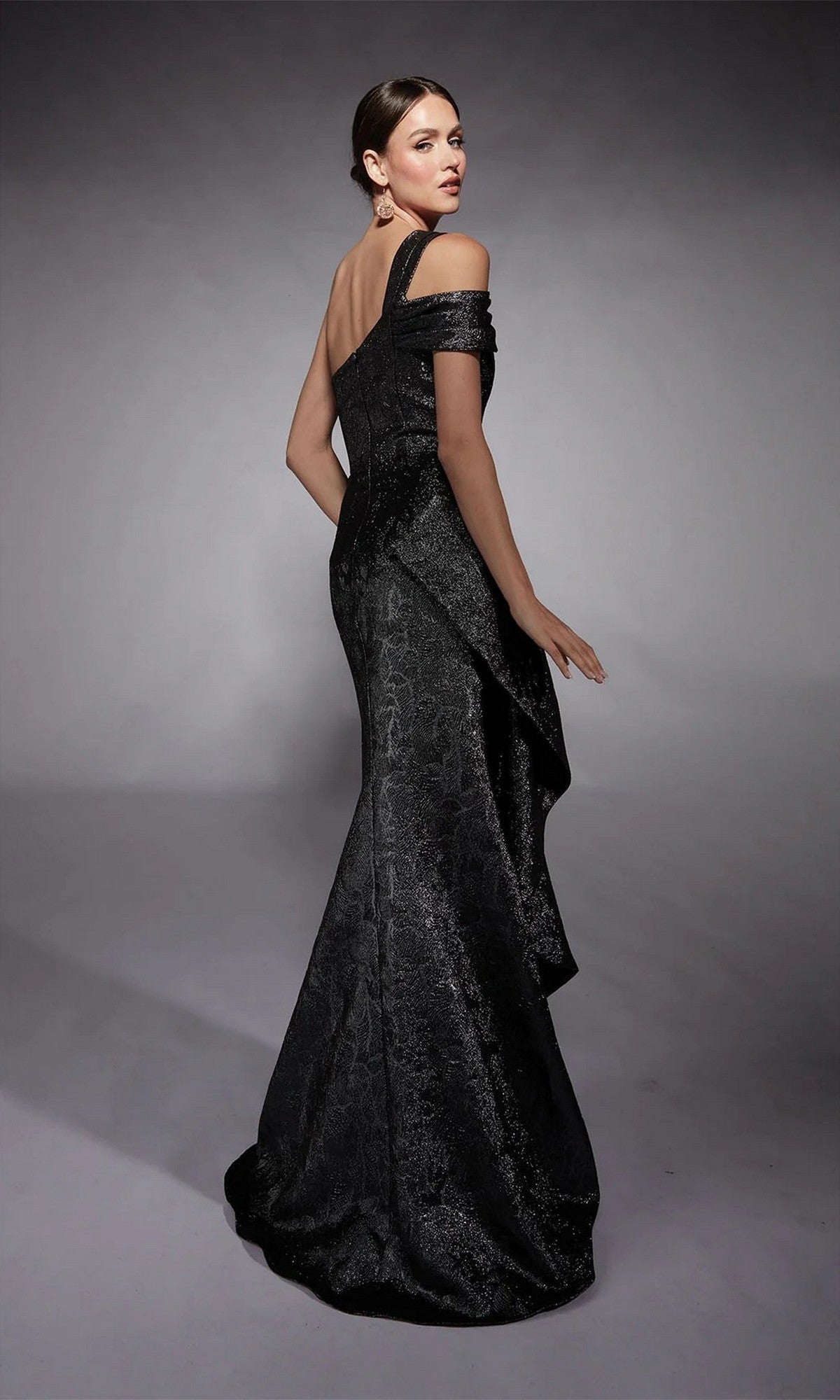 A woman models the Alyce 27734 long formal dress, an off-the-shoulder black gown with a textured pattern, standing against a plain gray background.